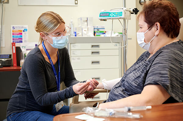 Health-care provider administering IV to patient in chair.