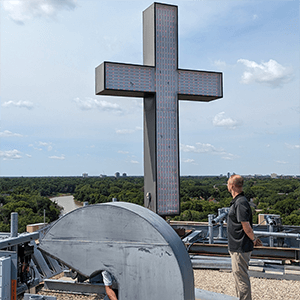 Man standing on Misericordia roof looking at large metal cross