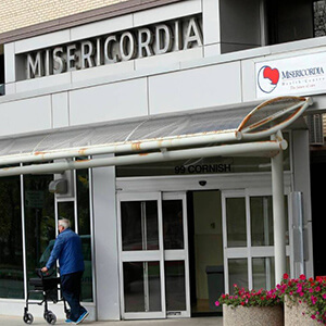 Man with walker on sidewalk in front of Misericordia Health Centre Cornish entrance.