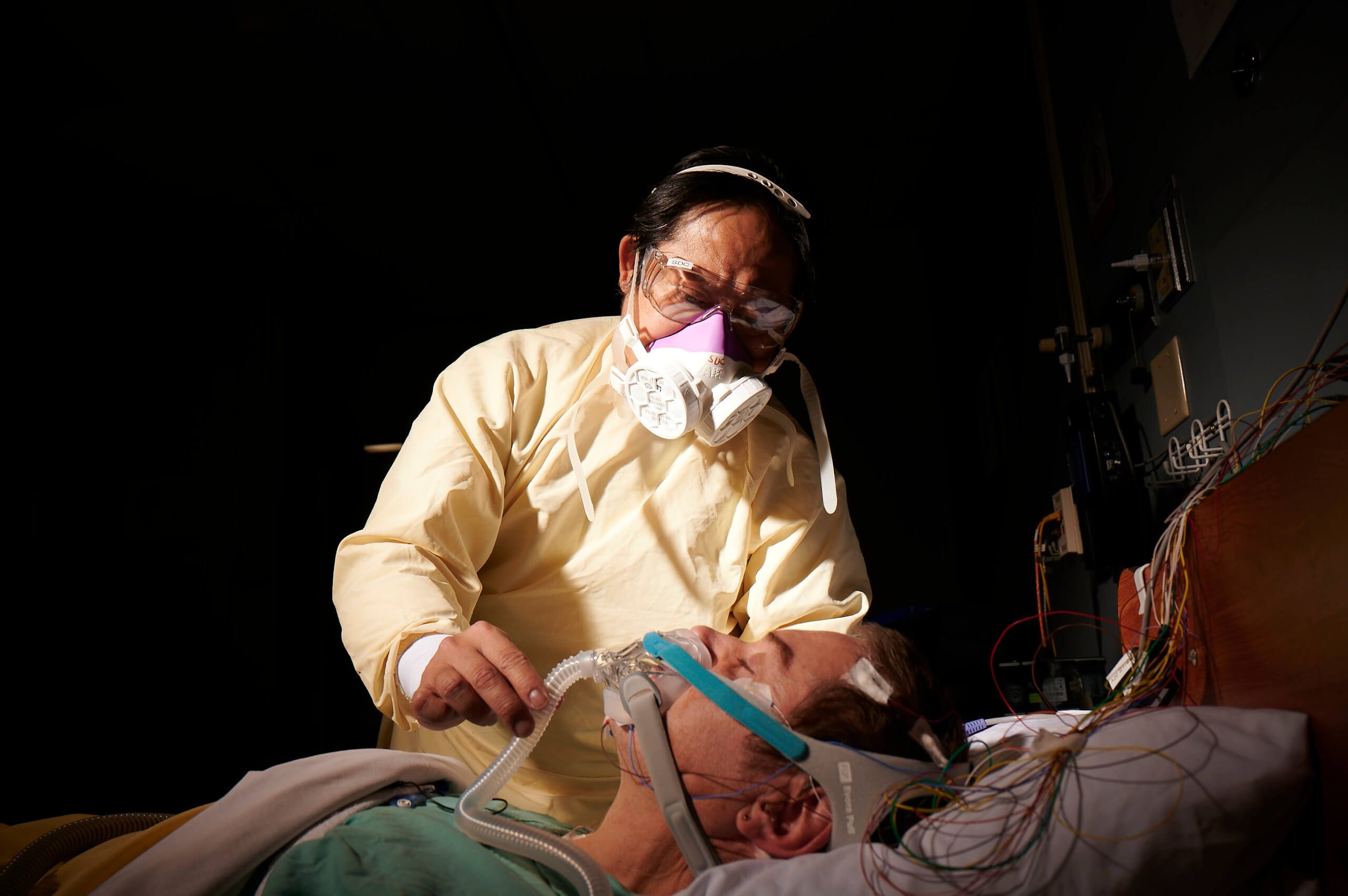 A sleep disorder technician adjusts a sleep aid machine on a patient.